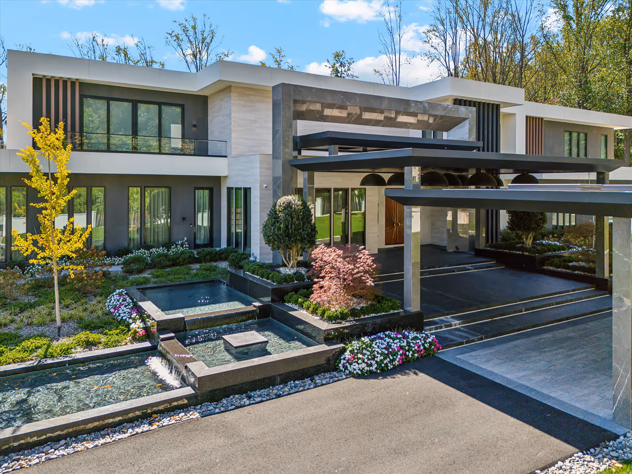 Modern two-story house with large windows, a covered driveway, landscaped garden, and tiered water features.