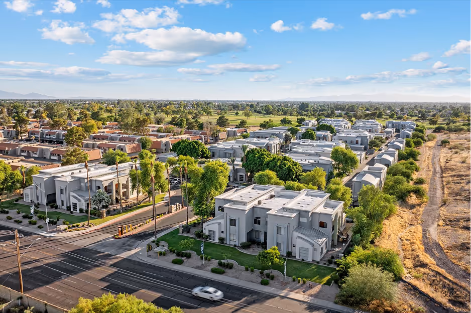 Aerial view of a suburban neighborhood with modern townhouses, lush greenery, and a clear blue sky.