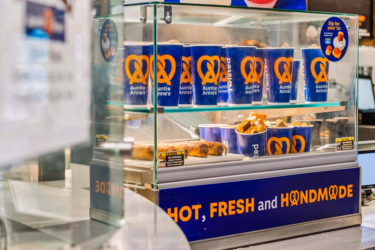 Glass display case with blue Auntie Anne's cups filled with pretzel sticks and a sign that reads Hot, Fresh and Handmade.