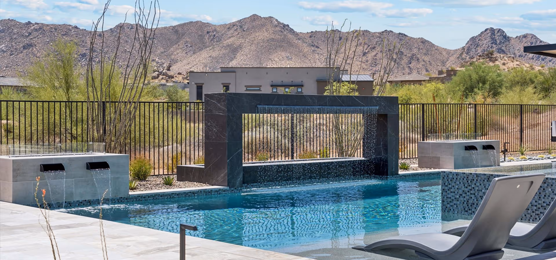 Modern swimming pool with built-in water features and lounge chairs set against a mountainous desert landscape.