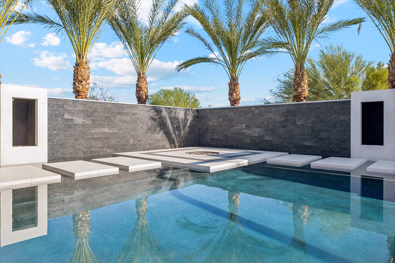 Modern outdoor pool with large floating white stepping stones and palm trees reflected in the water.