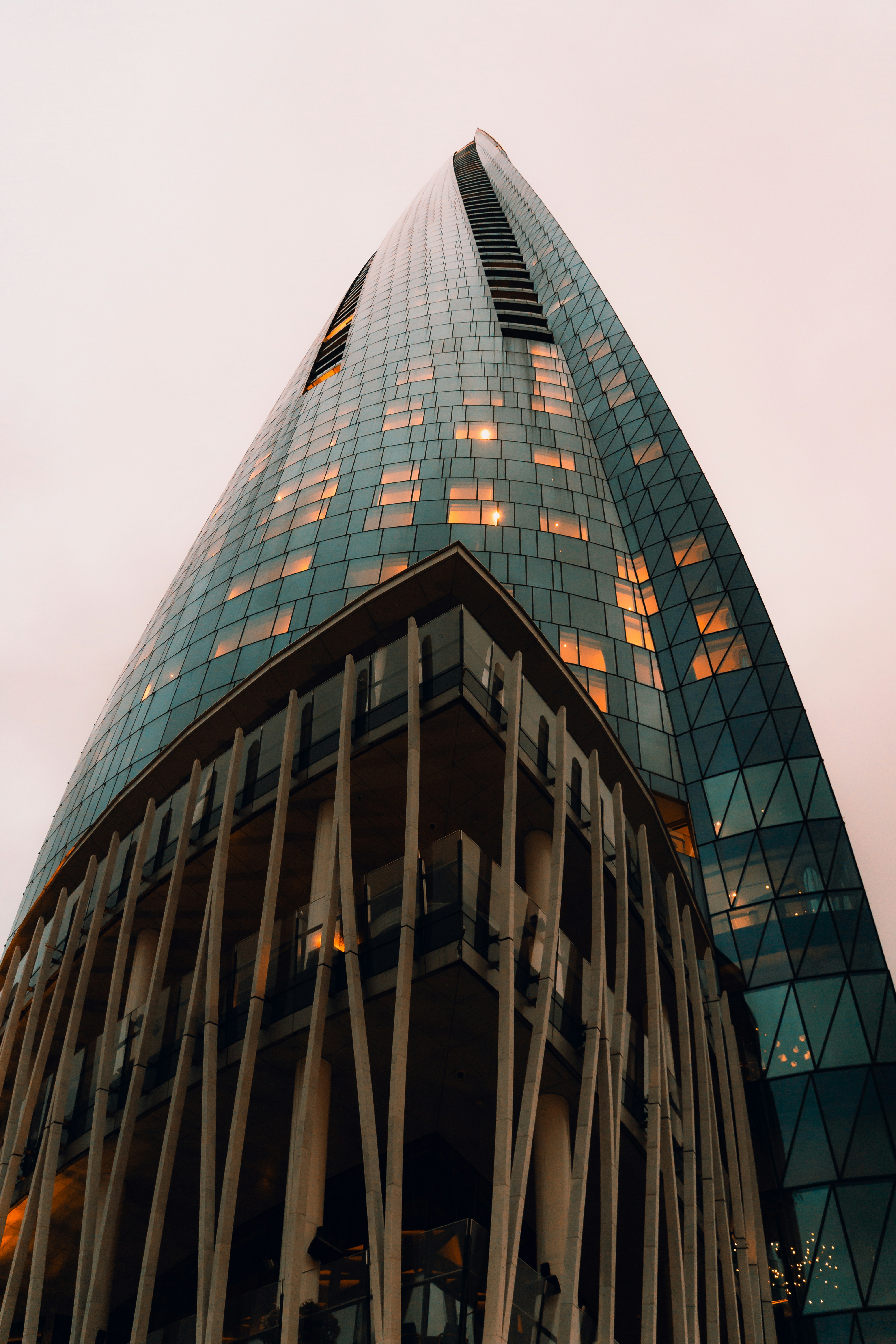 Low-angle view of a modern skyscraper with curved glass facade and illuminated windows at dusk.