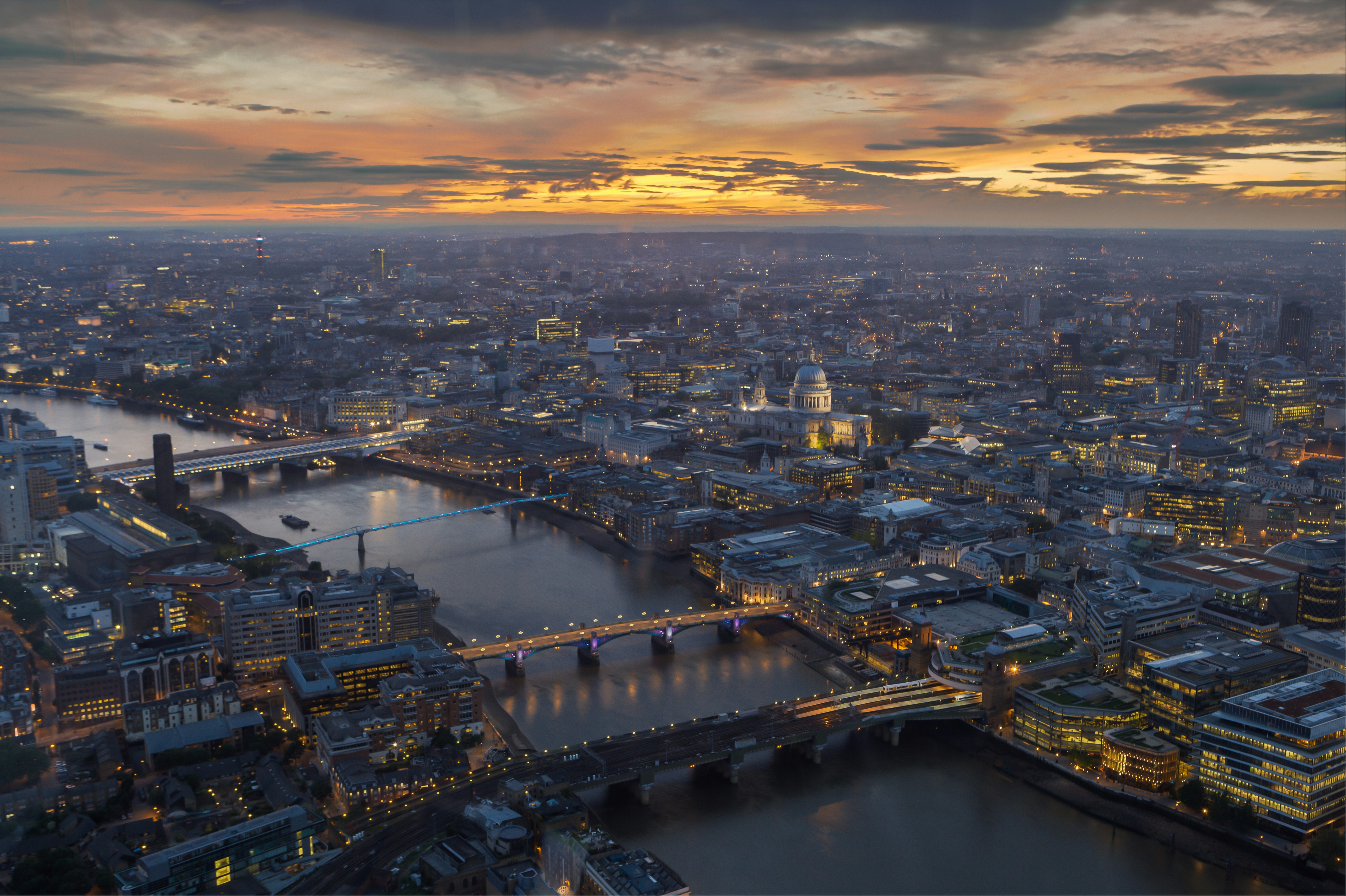Aerial view of a city at dusk with illuminated bridges crossing a river and a prominent domed building.