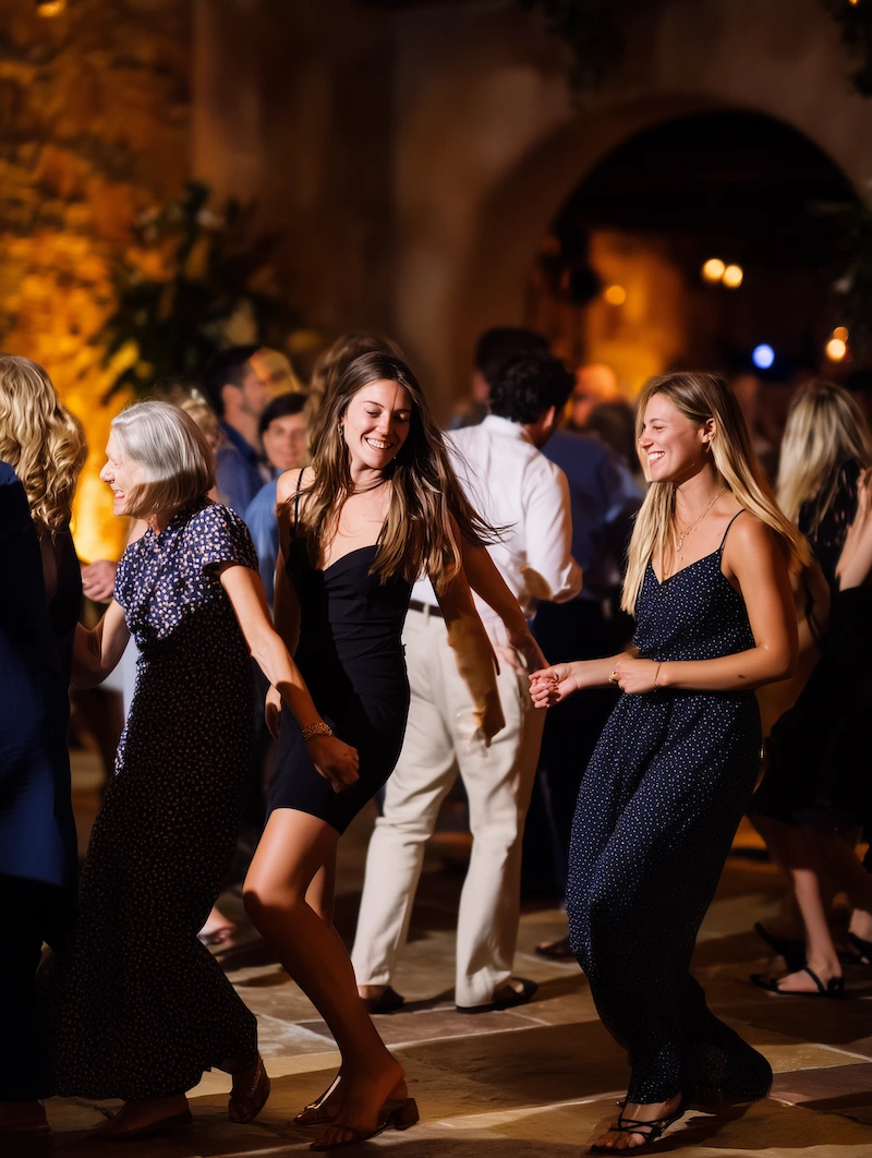 Three women dancing and smiling joyfully at a lively indoor event with warm lighting.