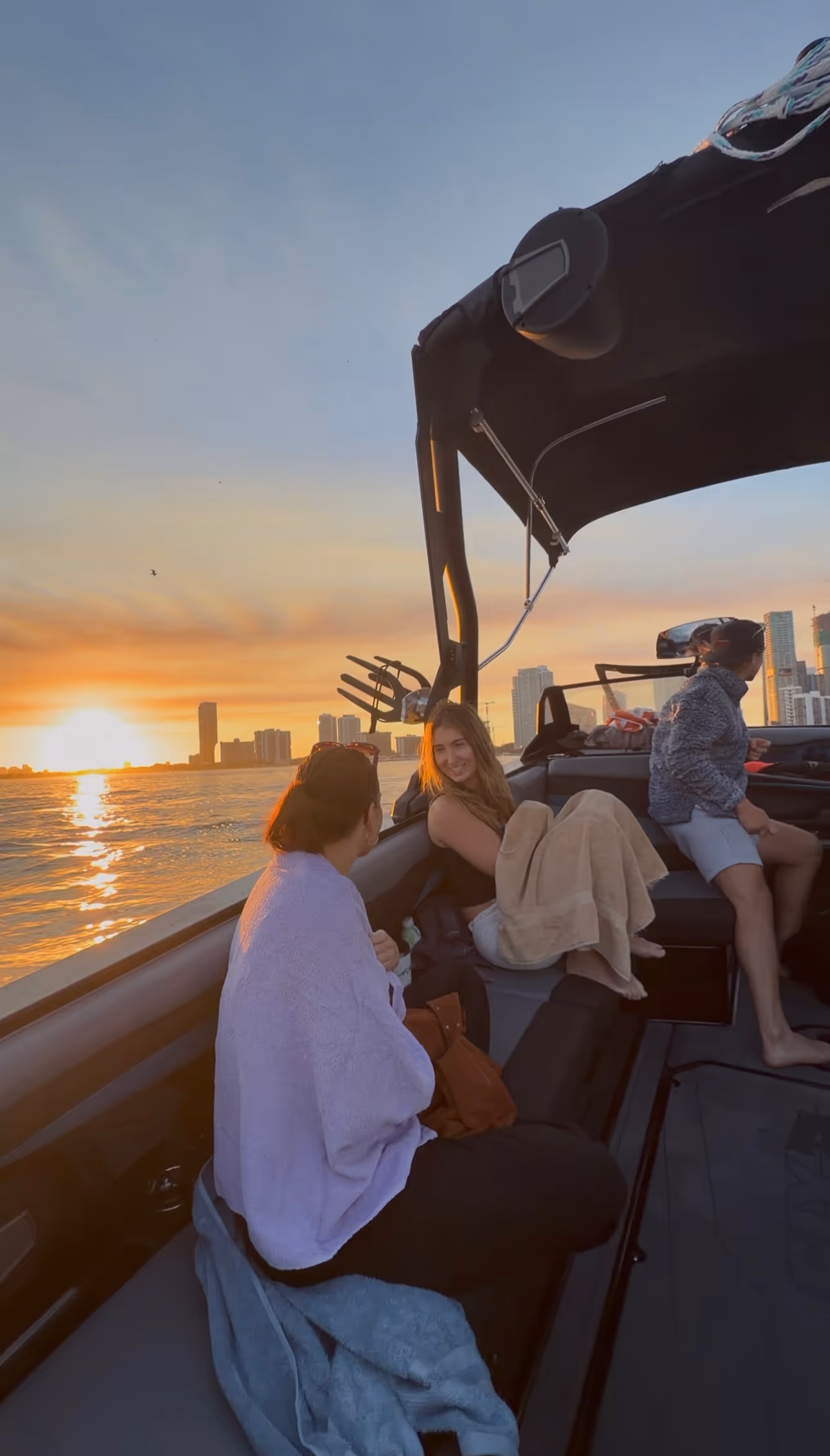 Three people relaxing on a boat during sunset with city skyline in the background.