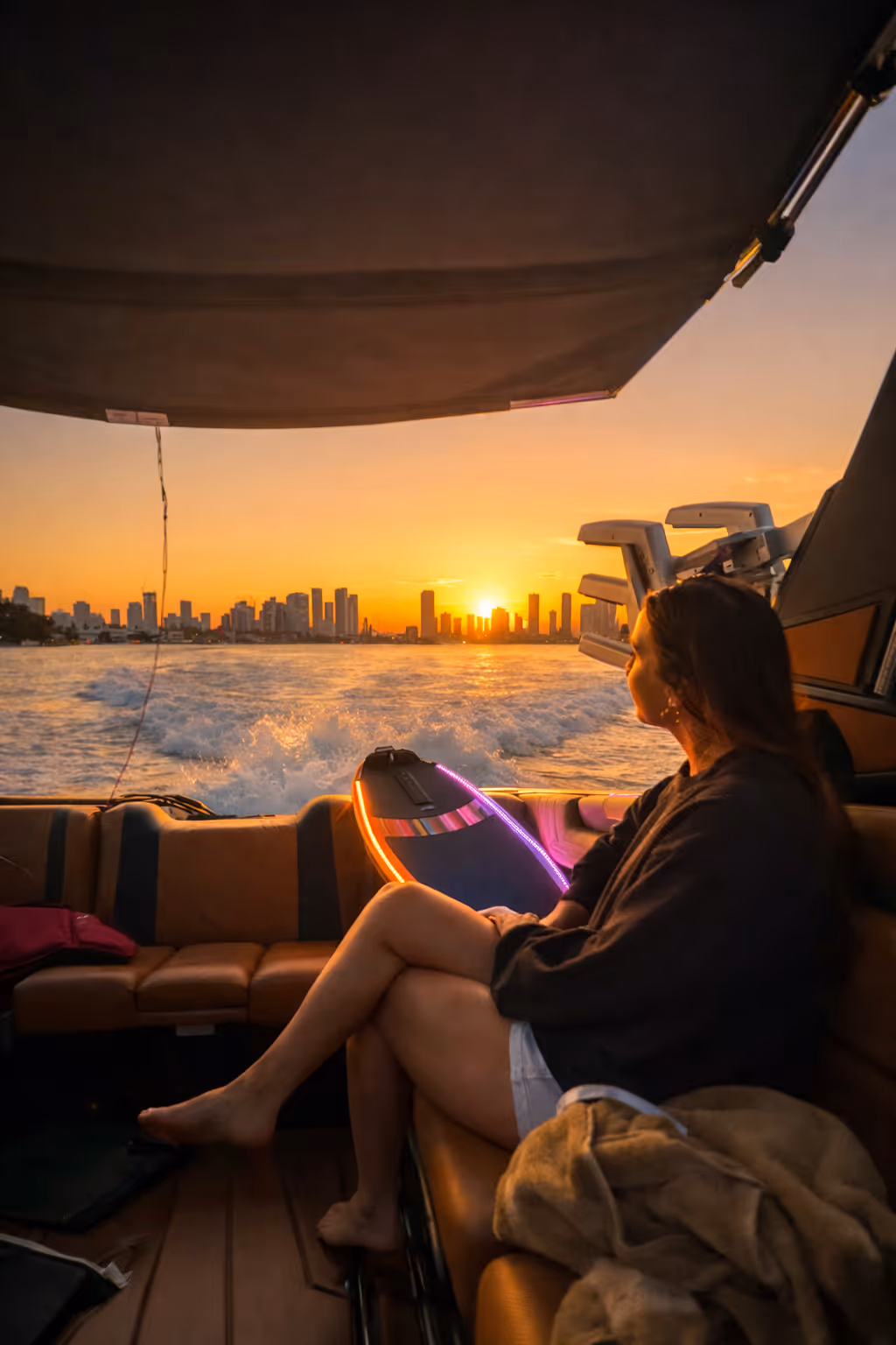 Three women relaxing on the bow of a boat cruising through a residential canal under a partly cloudy blue sky.