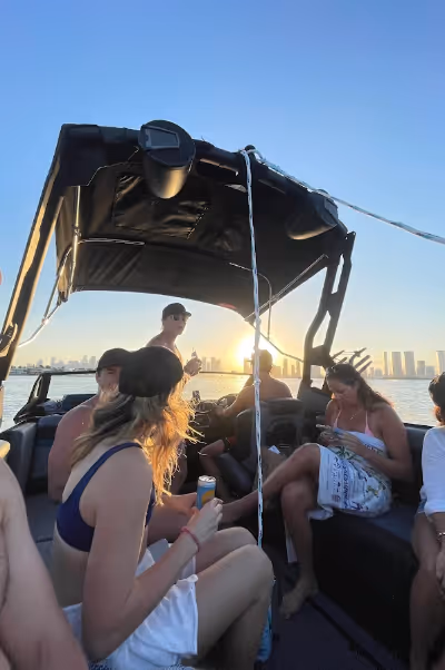 Group of people relaxing on a boat during sunset with a city skyline in the background.