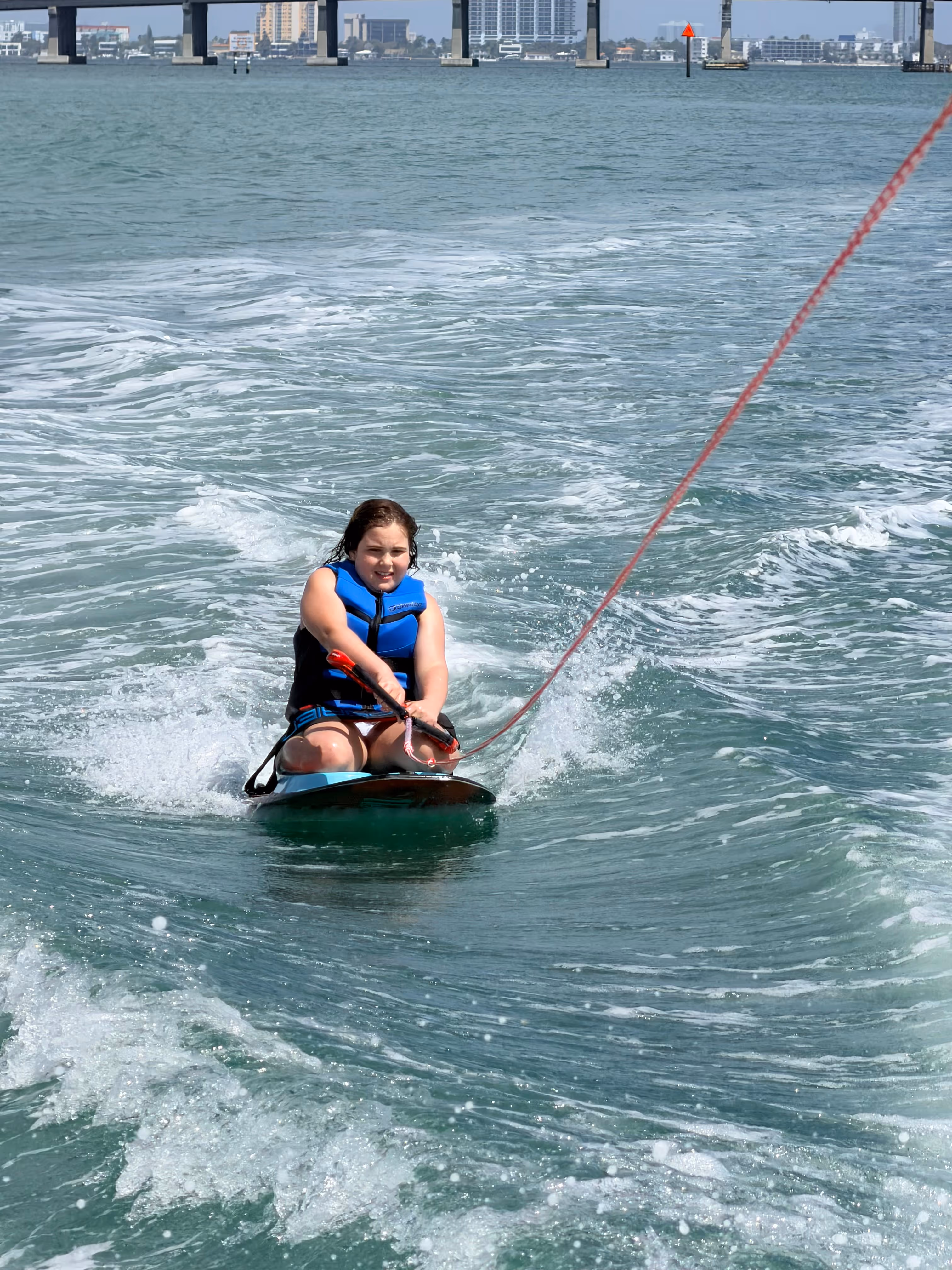 Man wakeboarding on water behind a boat, with another person steering the boat in the foreground.