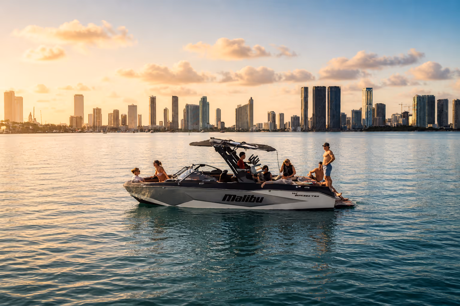 Group of people relaxing on a Malibu motorboat in calm blue water with Miami skyline under a partly cloudy sky.
