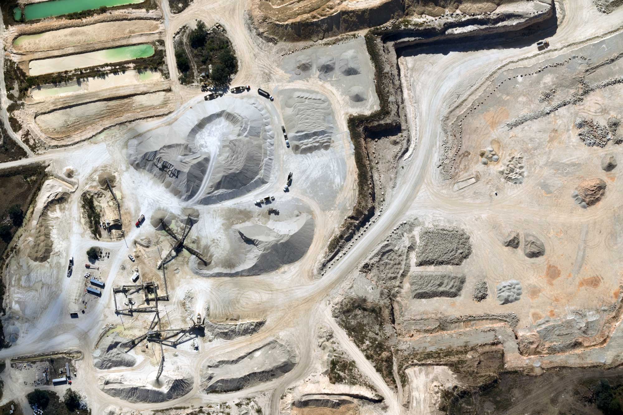 Aerial view of a quarry with large piles of sand and gravel, machinery, trucks, and dirt roads.