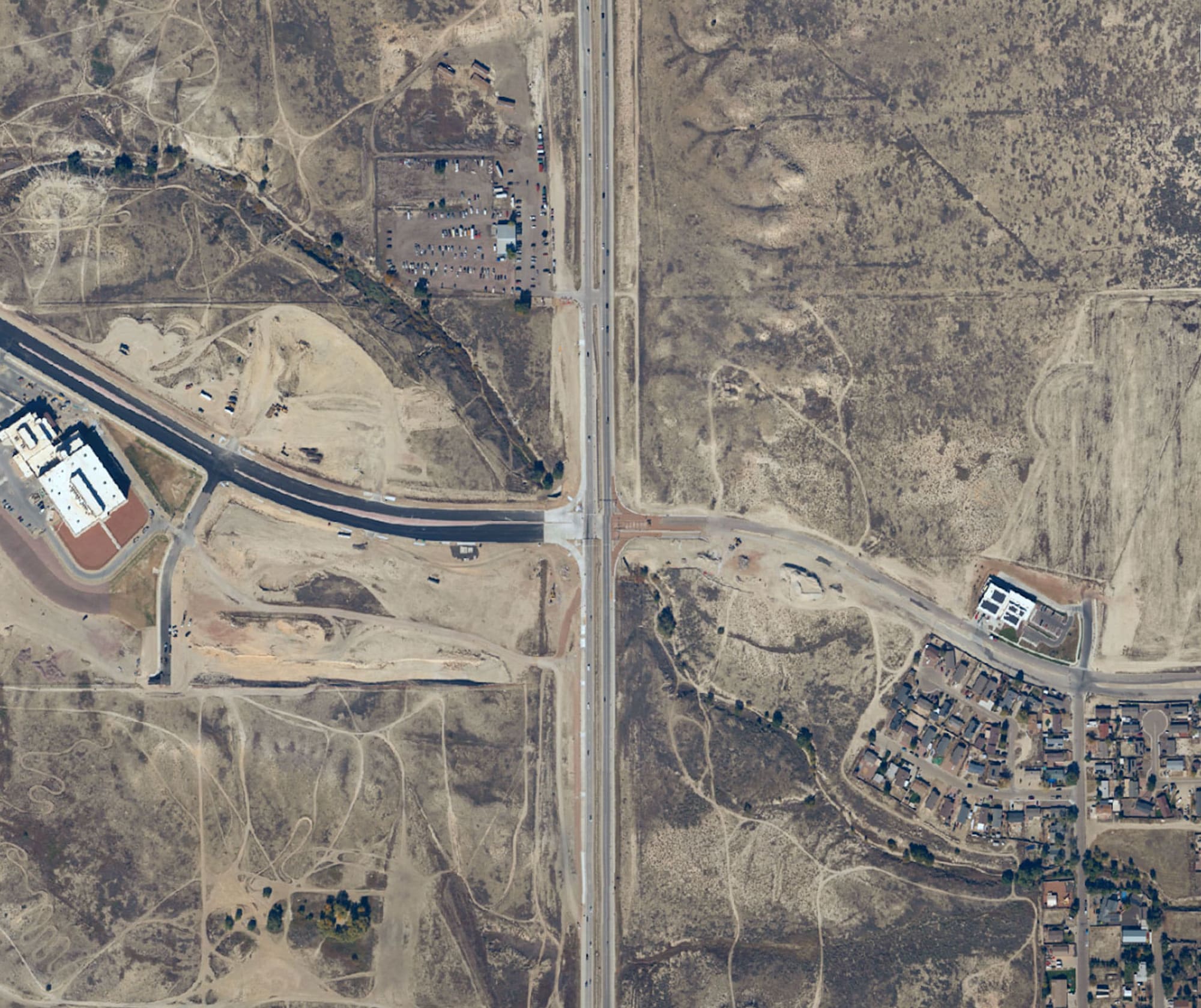 Aerial view of a highway intersection surrounded by patches of undeveloped land and a residential area.