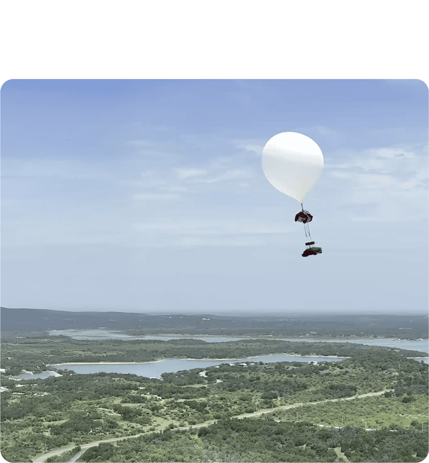 High-altitude white weather balloon with Near Space Labs' Swift robot floating over a green landscape with rivers and hills under a blue sky.