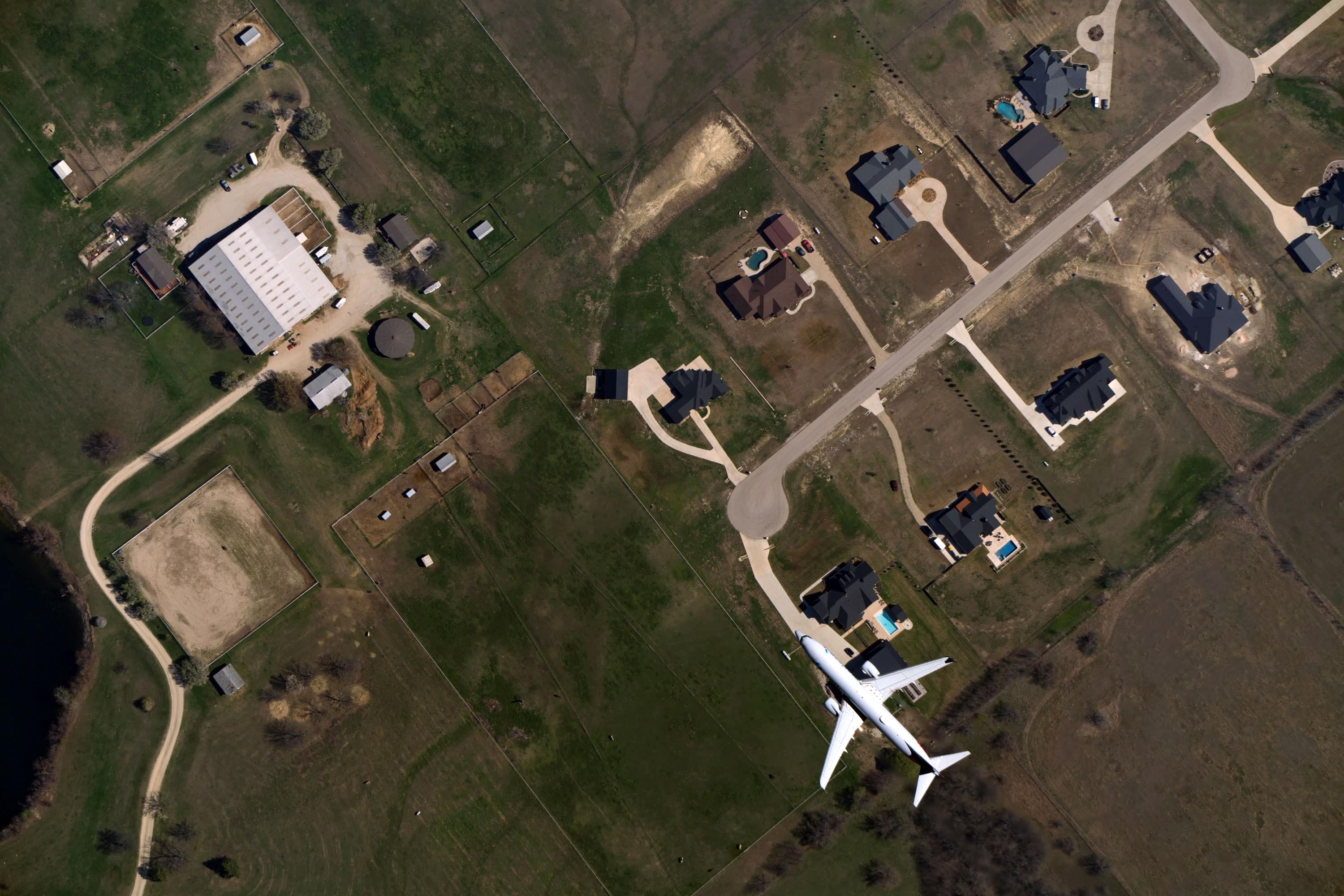 Aerial view of an airplane flying low over a rural neighborhood with houses, green fields, and farm buildings, captured from above by Near Space Labs' Swift robot.