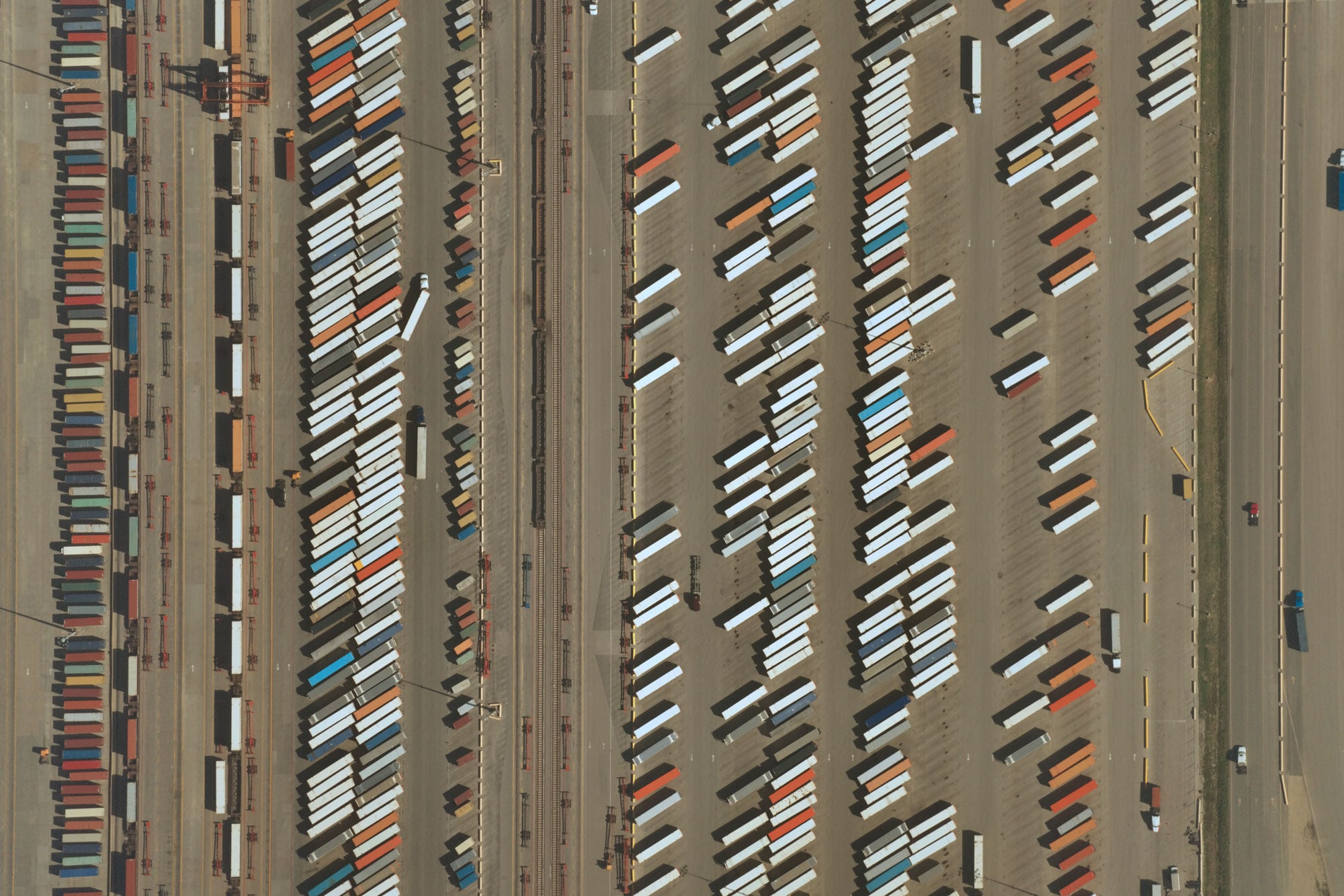 Aerial view of a shipping container yard with rows of colorful containers and trailers organized alongside rail tracks and roads.