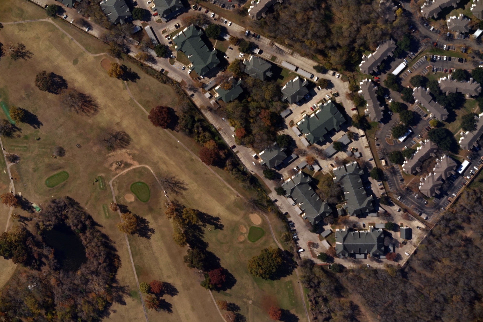 Aerial view showing a residential neighborhood adjacent to a golf course with green fairways, sand bunkers, trees, and a small pond.