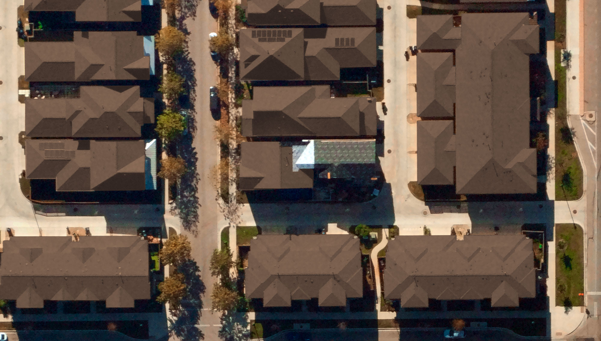 Aerial view of residential buildings with brown roofs and tree-lined streets in a suburban neighborhood.