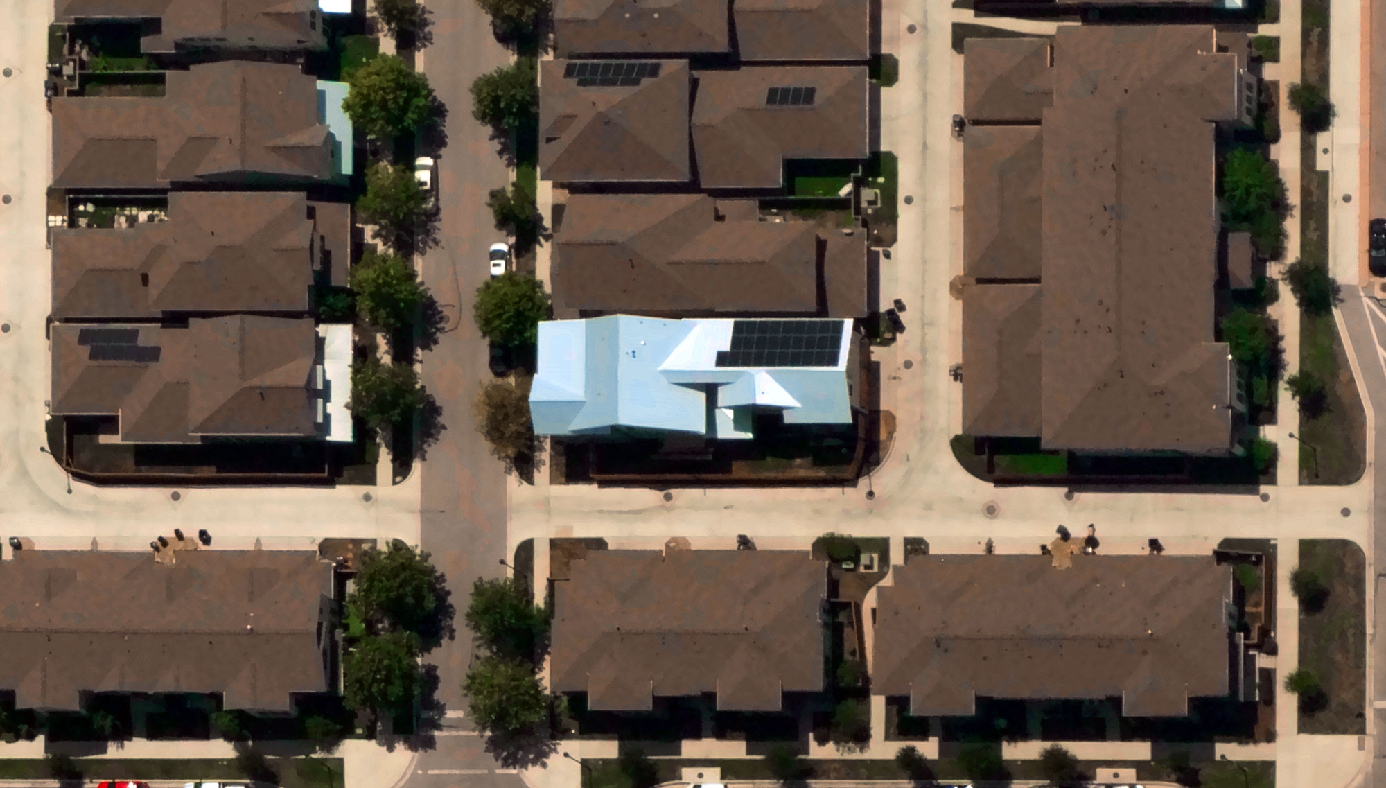 Aerial view of a neighborhood with multiple houses and a single house with a light blue roof and solar panels in the center.