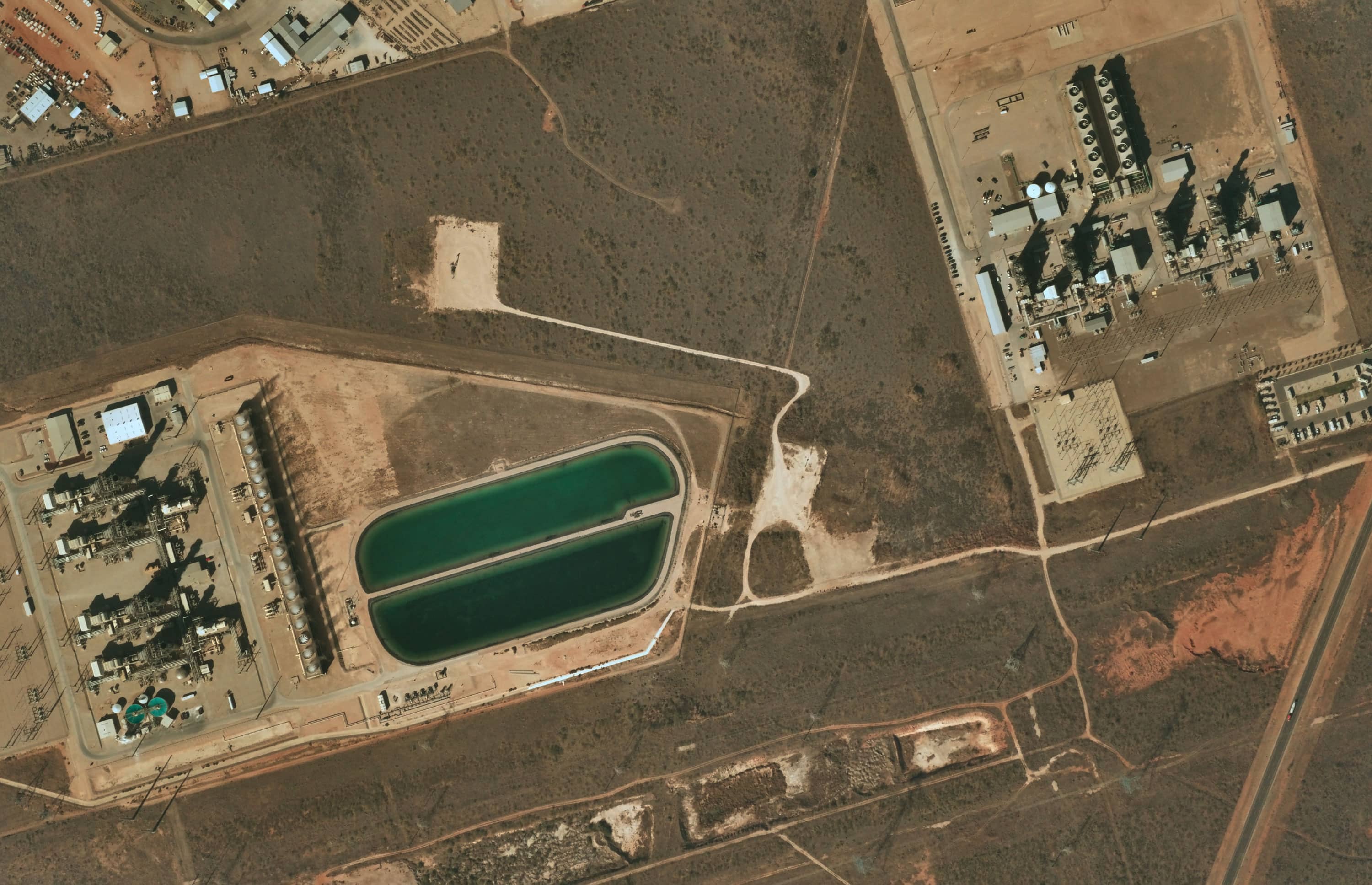 Aerial view of an industrial complex with large water tanks, buildings, equipment, and surrounding dirt roads.