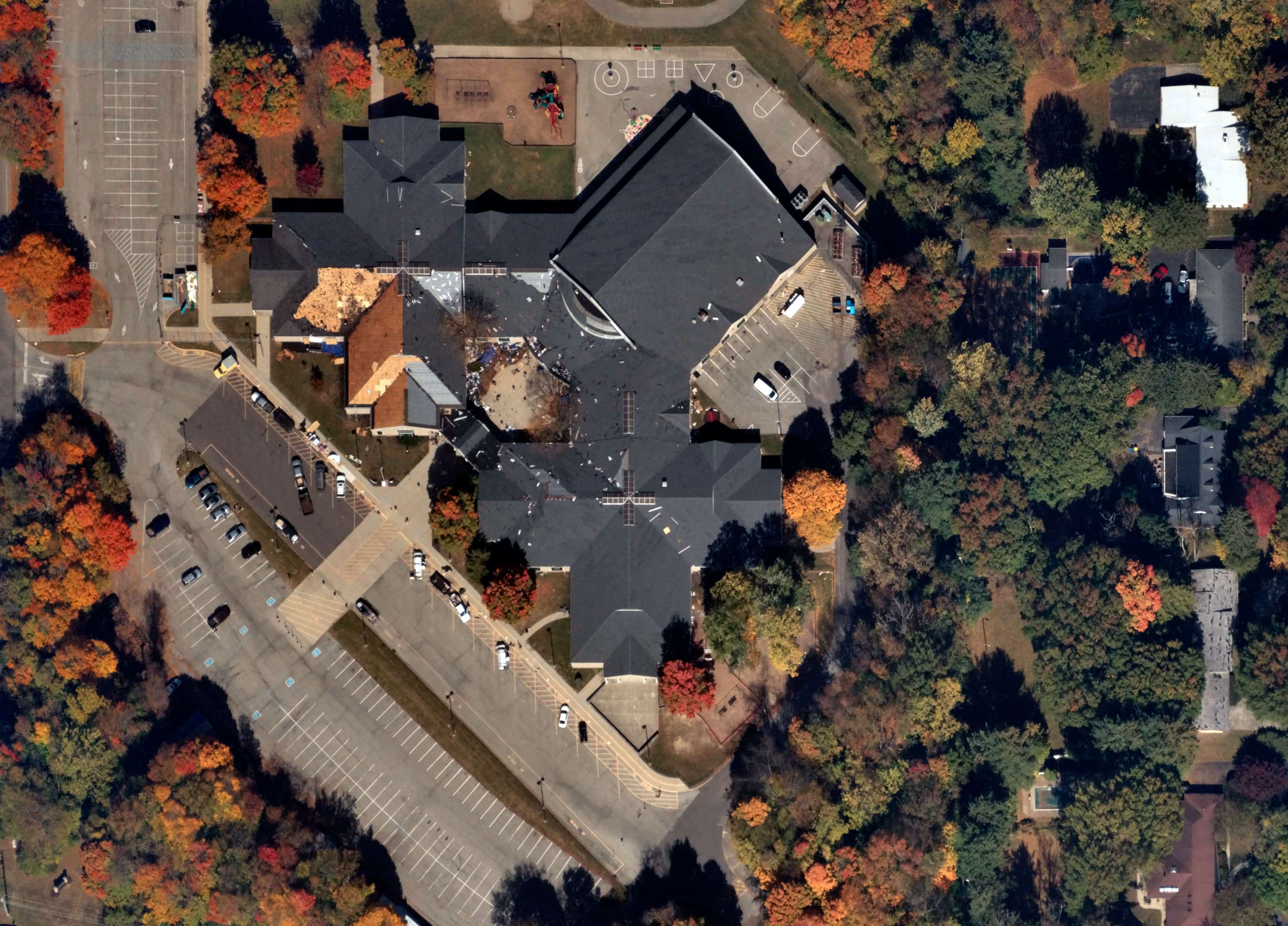 Aerial view of a large building with a dark roof surrounded by autumn-colored trees and adjacent parking lots.
