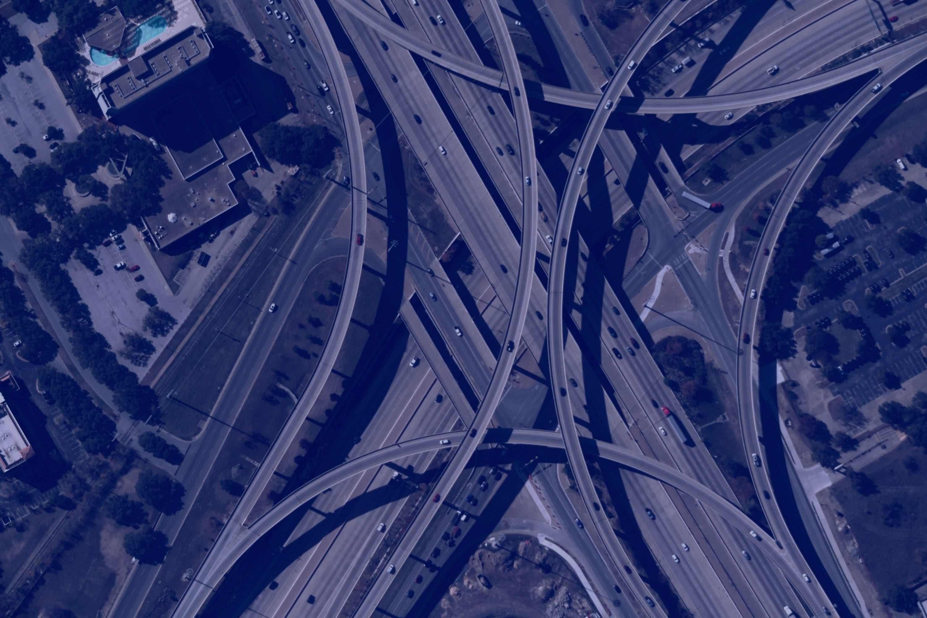 Branded, blue-tinted aerial view of a complex highway interchange with multiple overpasses and vehicles traveling in various directions.