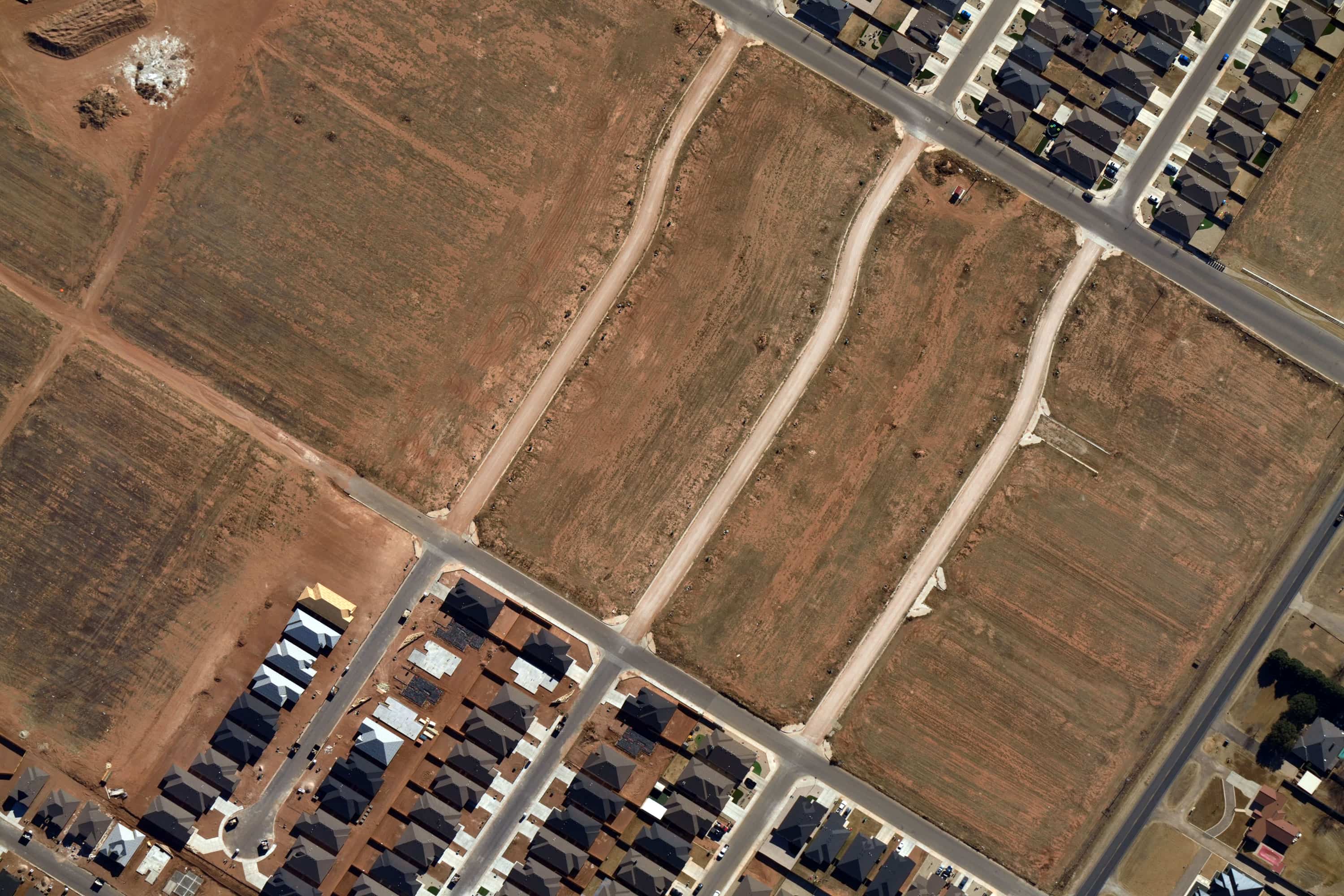 Aerial view of a residential area with houses and several adjacent empty lots with dirt roads.