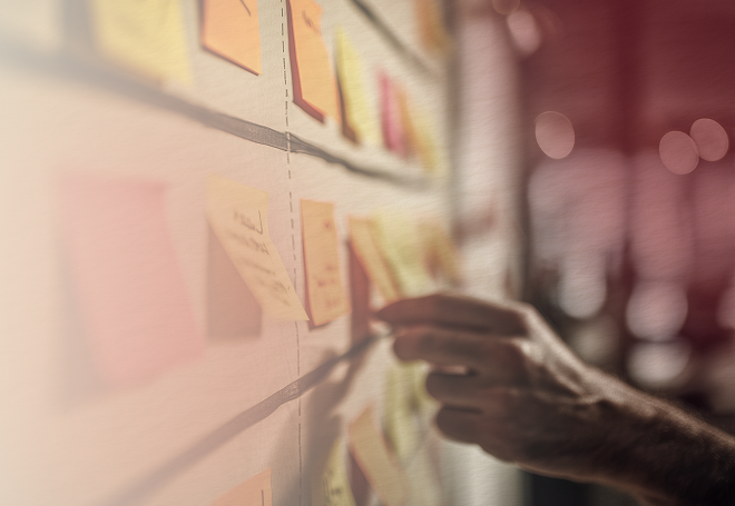 Hand arranging colorful sticky notes on a whiteboard with grid lines in a blurred office setting.