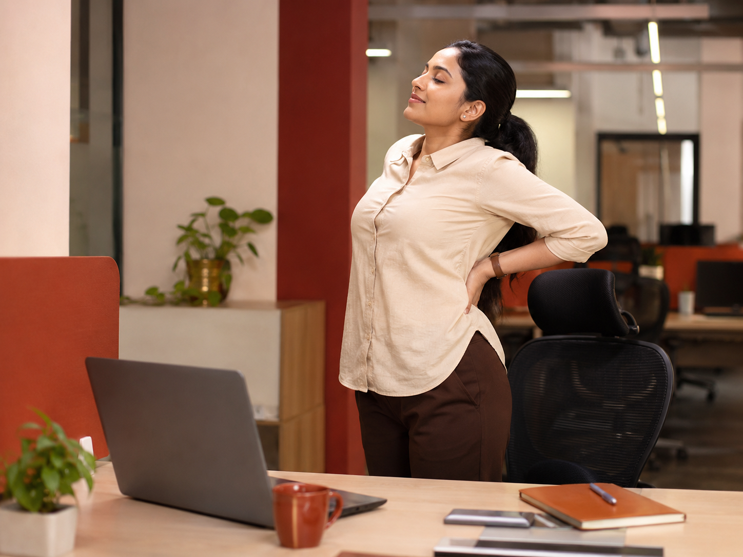 An office worker standing to stretch their lower back beside a desk, illustrating staying active with back pain.