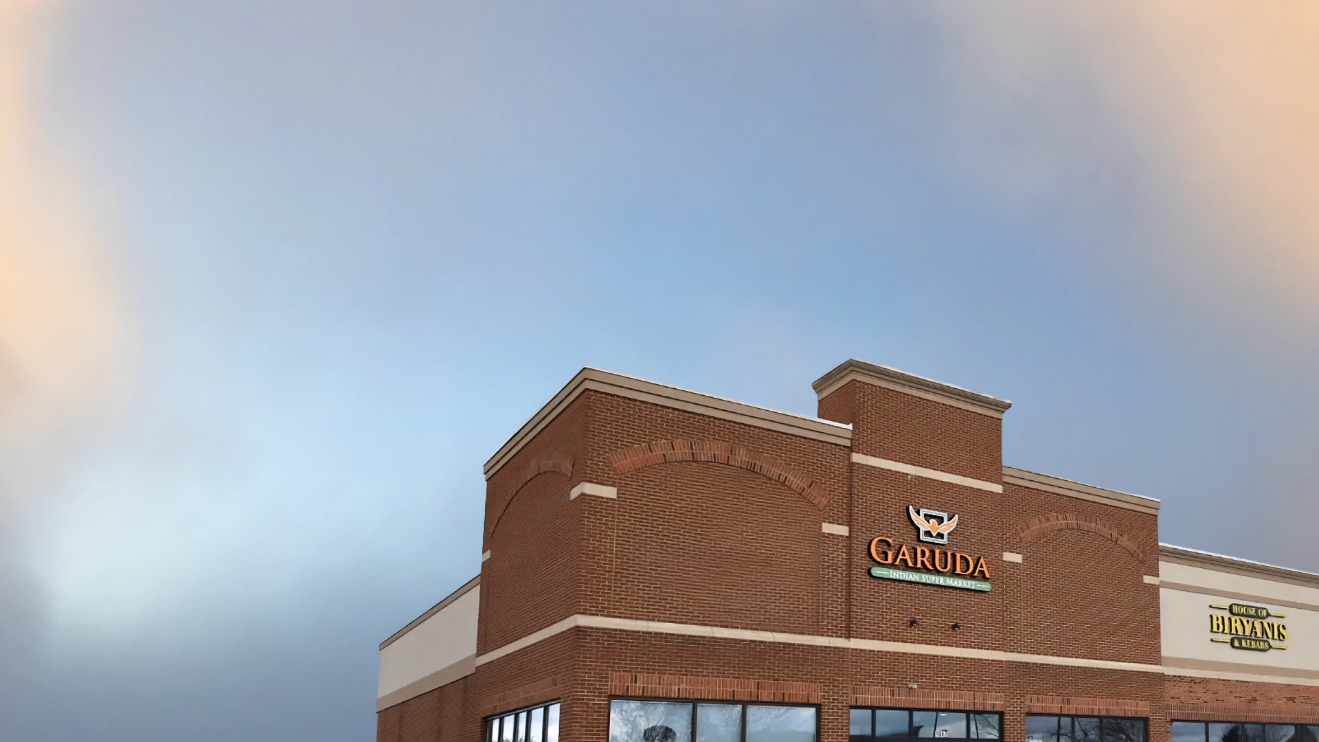 Brick building with signs for Garuda Indian Super Market and House of Biryanis & Kebabs under a clear sky.
