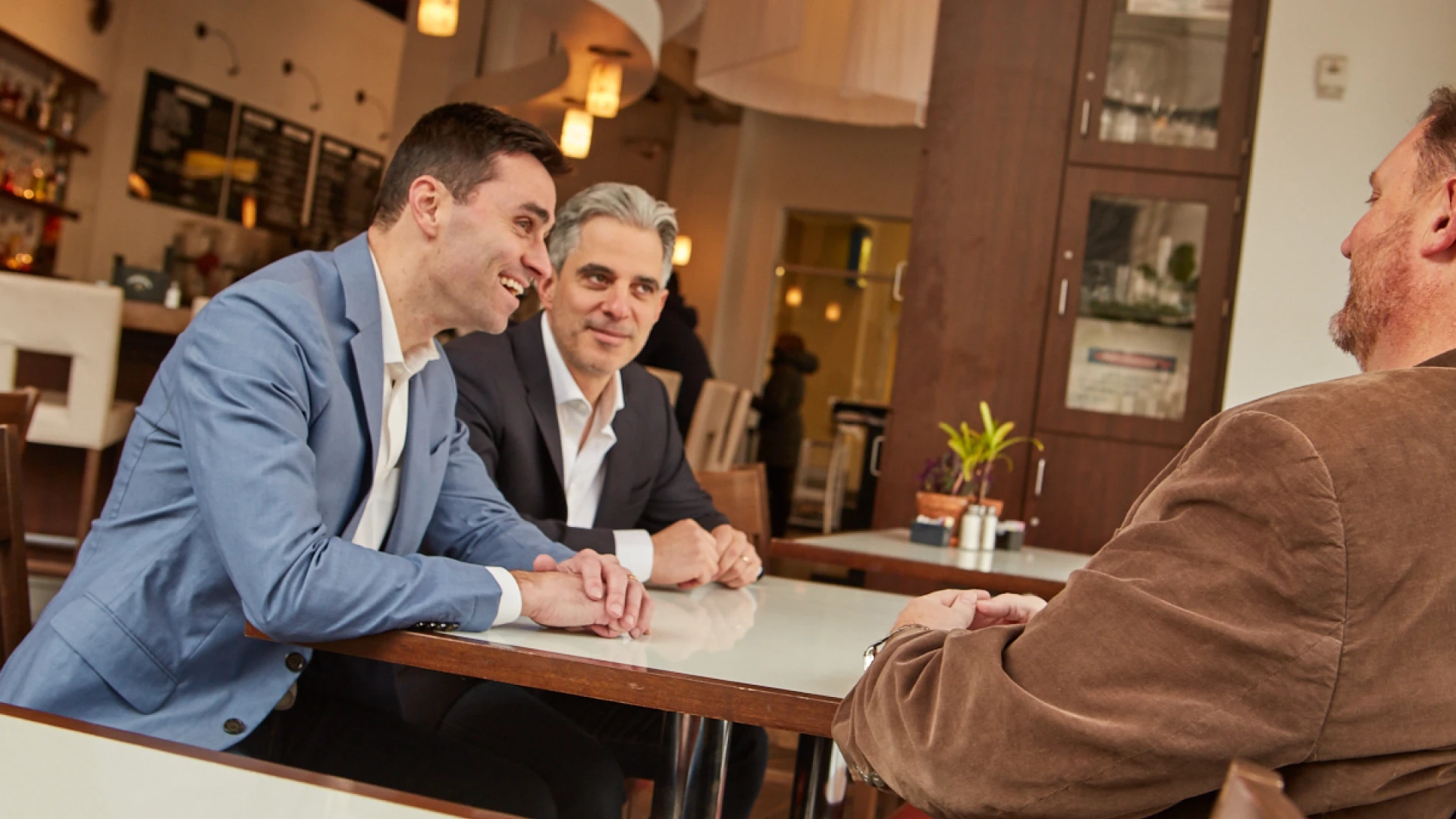Three men in a restaurant engaged in a cheerful conversation around a table.