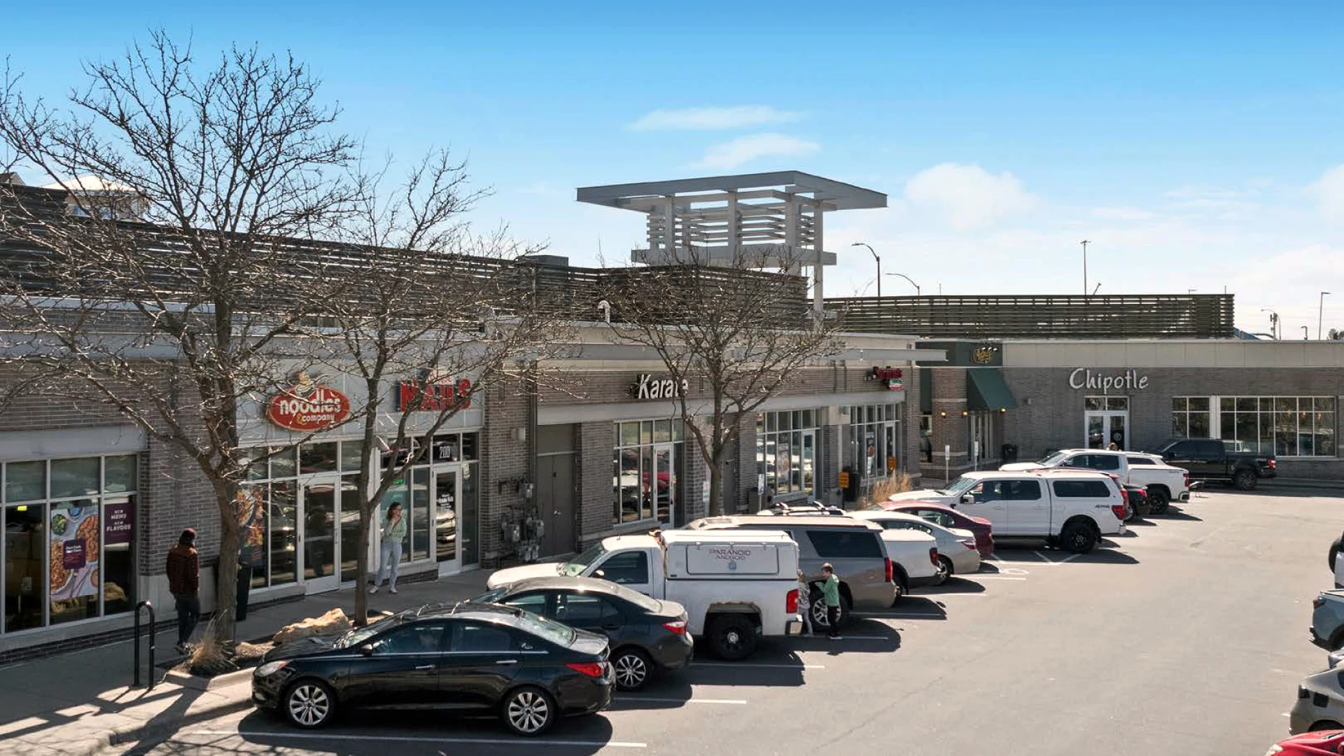 Three men sitting at a table in a restaurant engaged in a conversation, two facing the camera and one with his back to the camera.