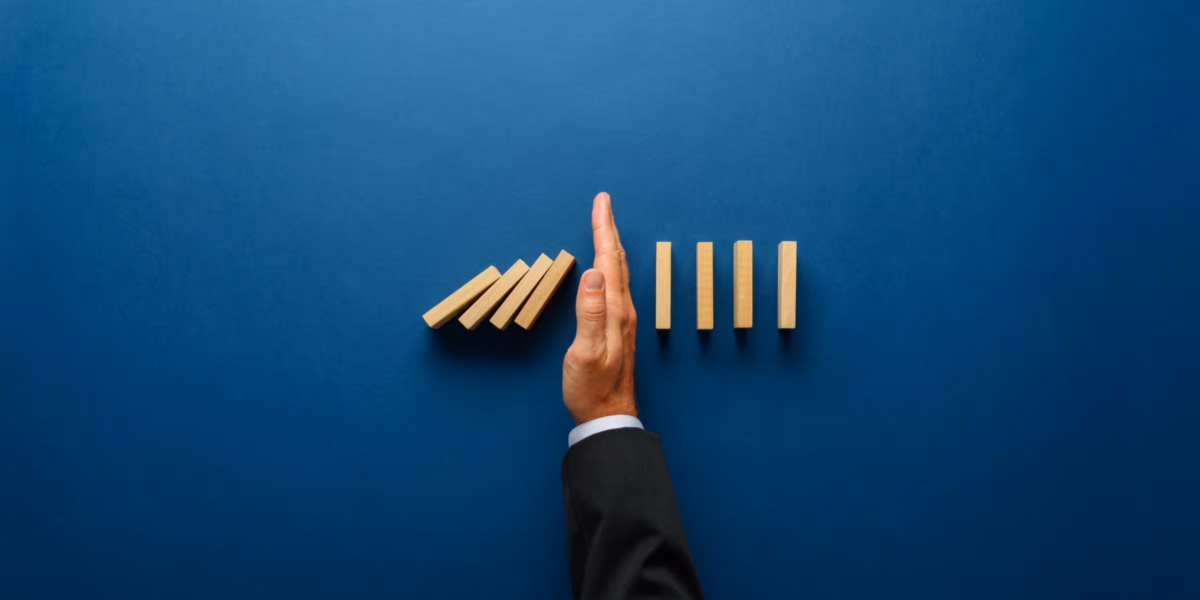 hand stopping falling dominoes representing risk management in trading