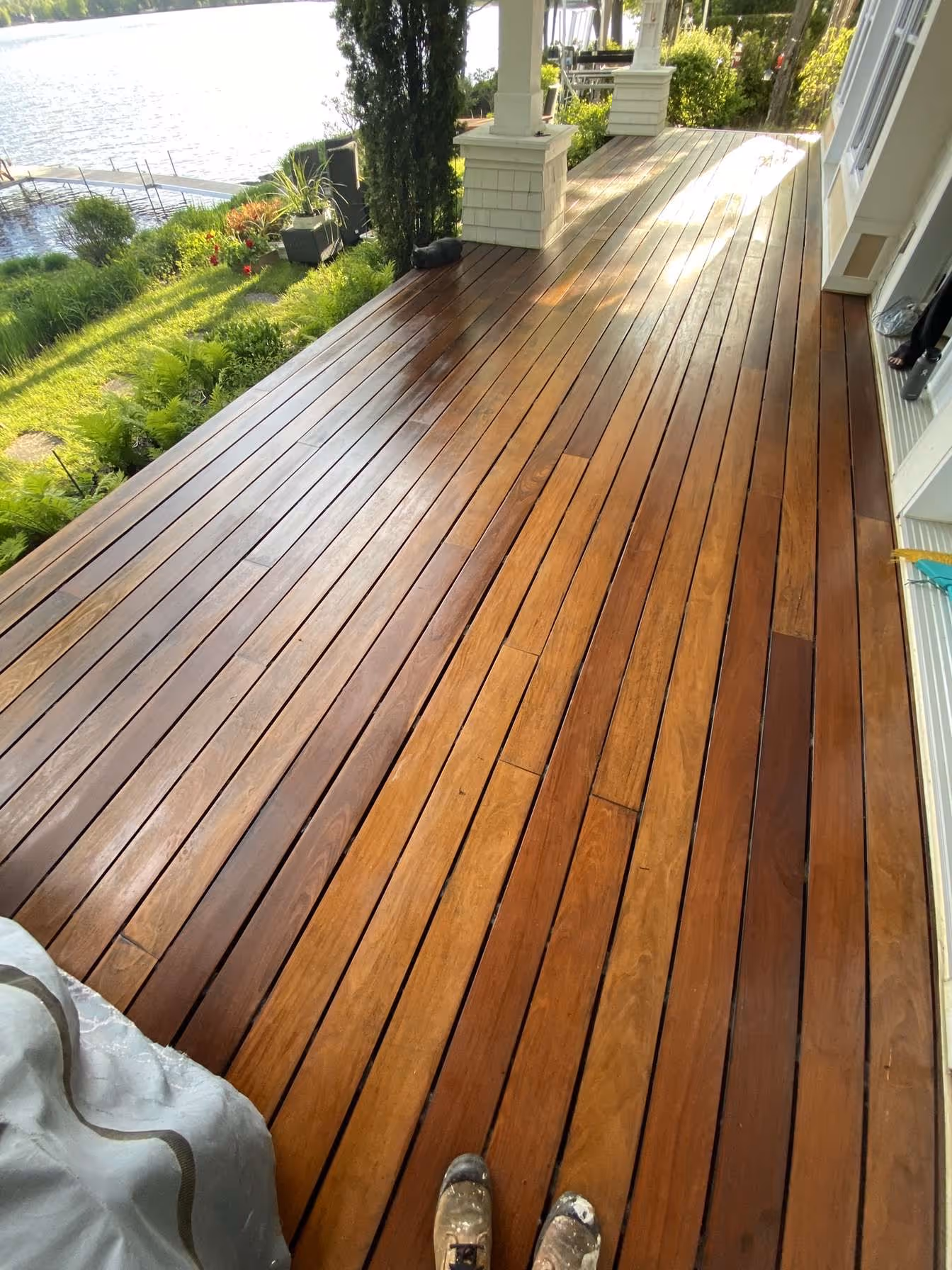 Vue d'une terrasse en bois poli avec une vue sur un lac et un jardin verdoyant à côté.
