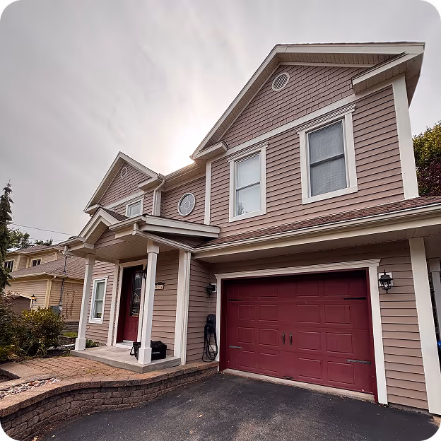 Maison à deux étages avec un garage rouge et un porche avec colonnes sous un ciel nuageux.