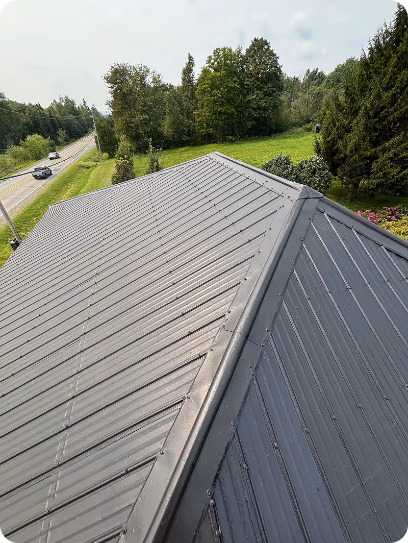 Vue aérienne d’un toit en métal gris avec une route et des arbres verts en arrière-plan.
