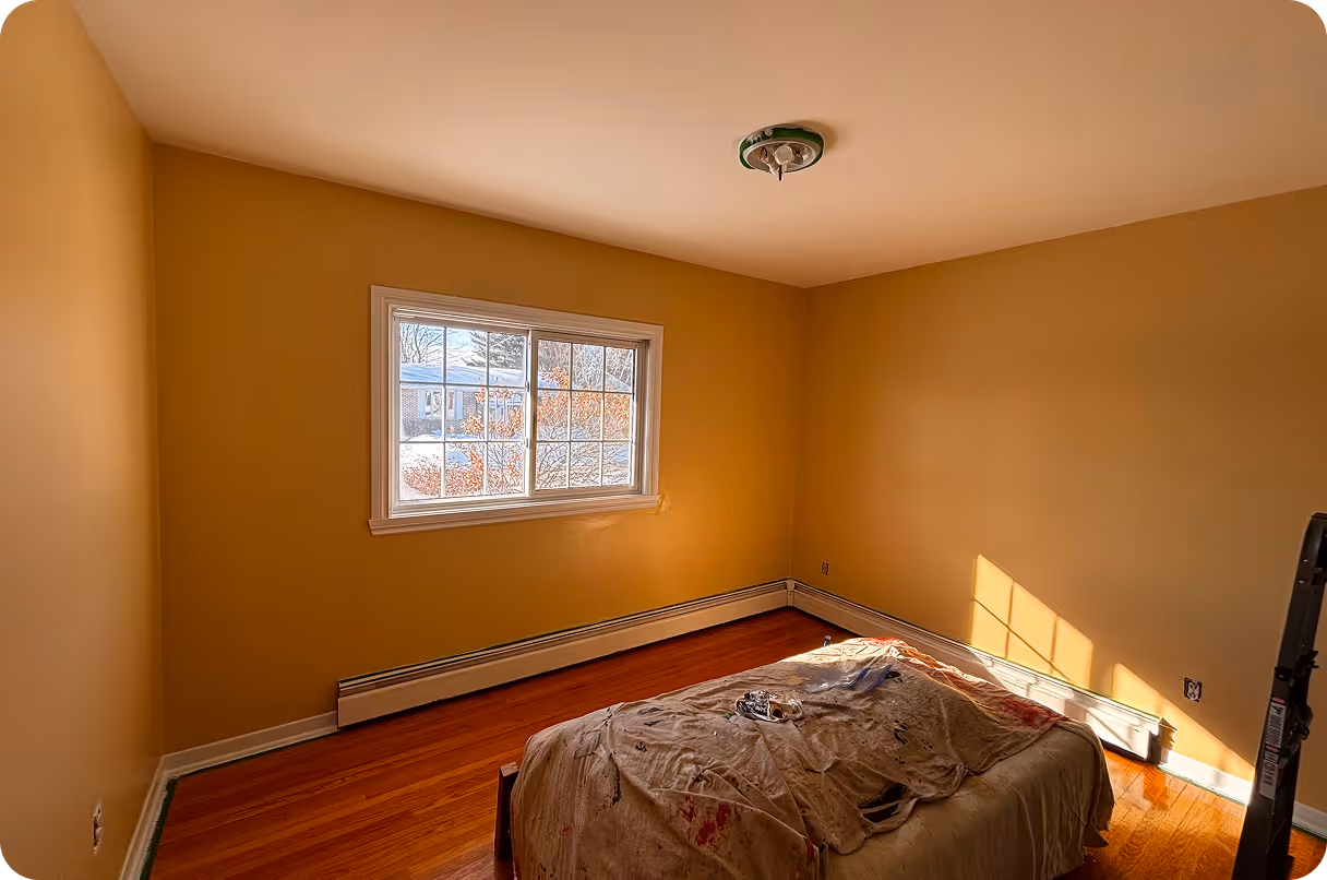Chambre vide avec murs jaunes, plancher en bois et fenêtre laissant entrer la lumière naturelle.