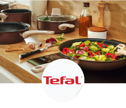 Poêles de cuisine Tefal avec légumes sautés et ingrédients sur un comptoir en bois.