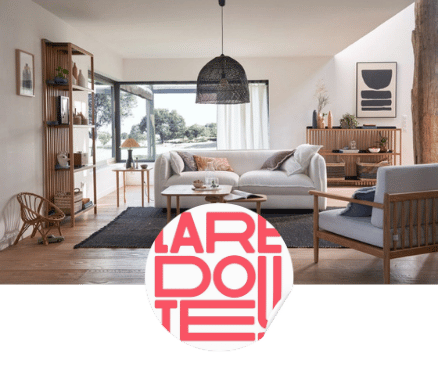 Salon lumineux avec grand canapé gris, fauteuil en bois, table basse ronde et grande baie vitrée donnant sur un jardin.