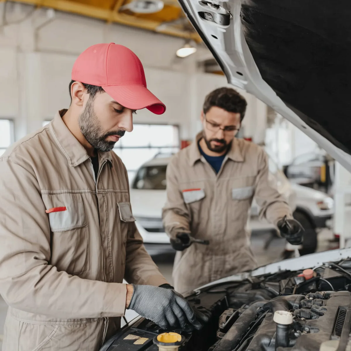 Zwei Mechaniker in Overalls inspizieren den Motorraum eines Autos in einer Werkstatt.