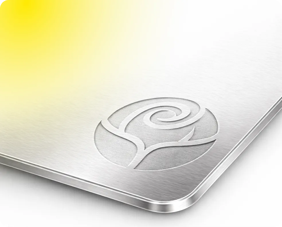 Close-up of a brushed metal surface with an embossed stylized rose design and a soft yellow light reflection on the upper left corner.