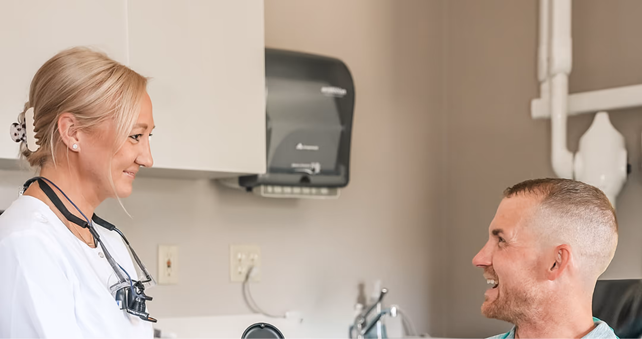 Female healthcare professional in white coat smiling and talking to a male patient in a medical office.