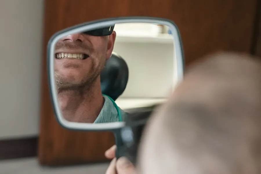 Reflection of a smiling man wearing sunglasses seen through a rearview mirror.