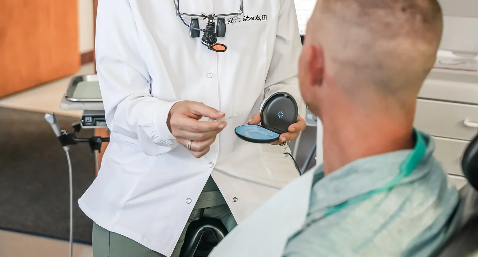 Dentist showing a clear dental aligner to a seated patient in a dental office.