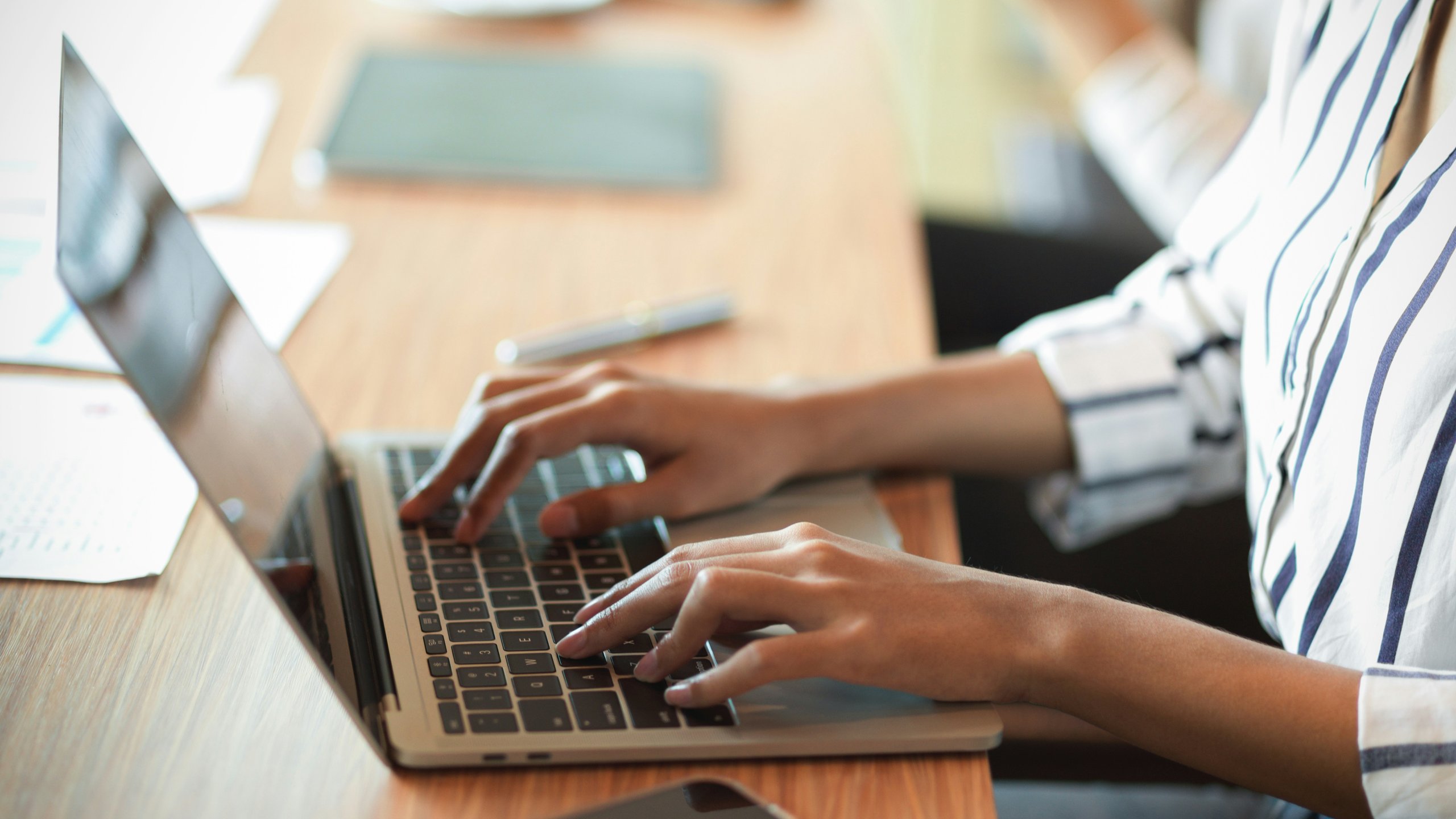 Women's hands on a desk, typing on a laptop.