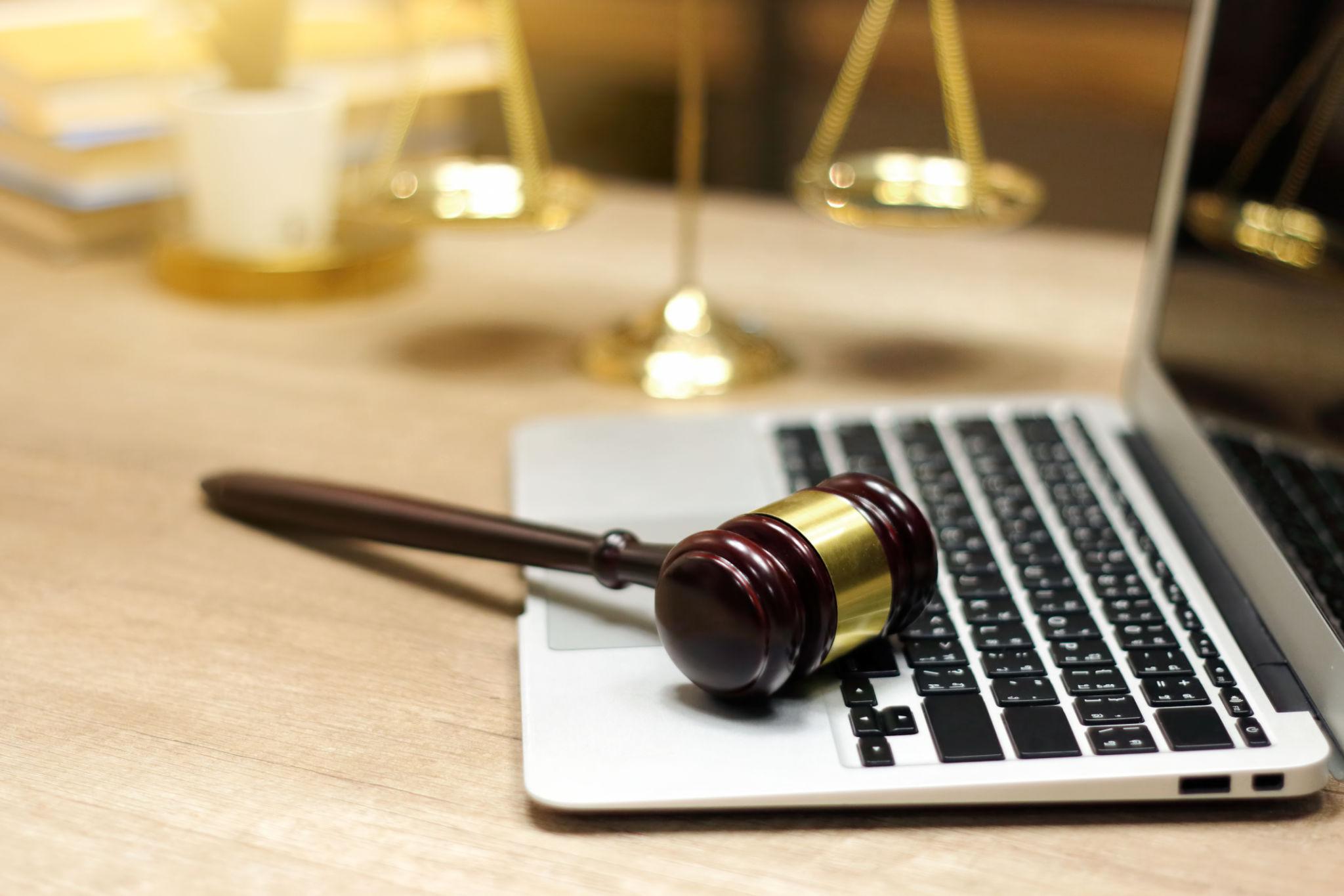 Laptop with a gavel laying on the keyboard. Gold justice scales in the back ground.
