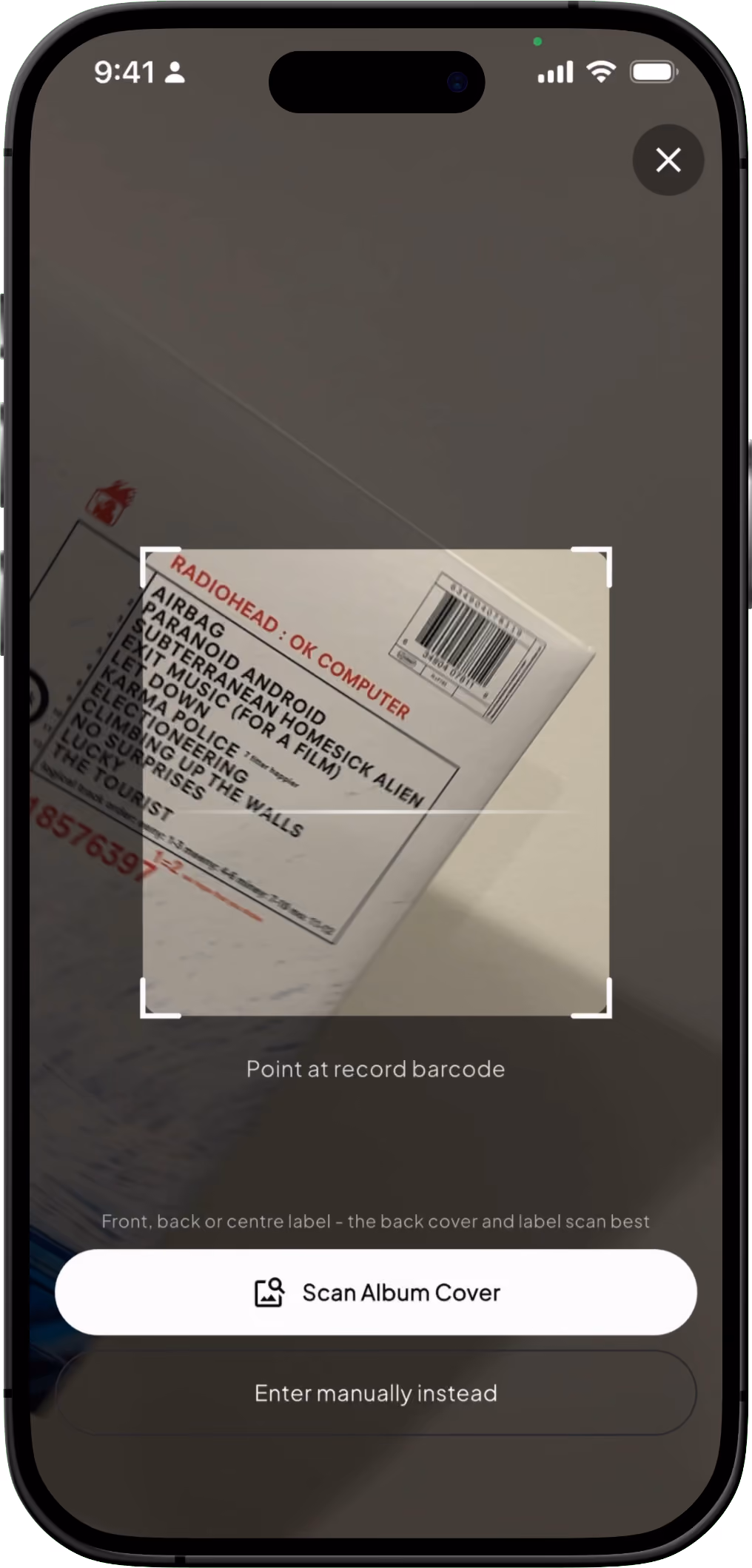 Smartphone screen shows a barcode scanner app pointing at the back cover of Radiohead's OK Computer album, listing tracks such as 'Airbag,' 'Paranoid Android,' and 'Subterranean Homesick Alien.' Buttons read 'Scan Album Cover' and 'Enter manually instead.'