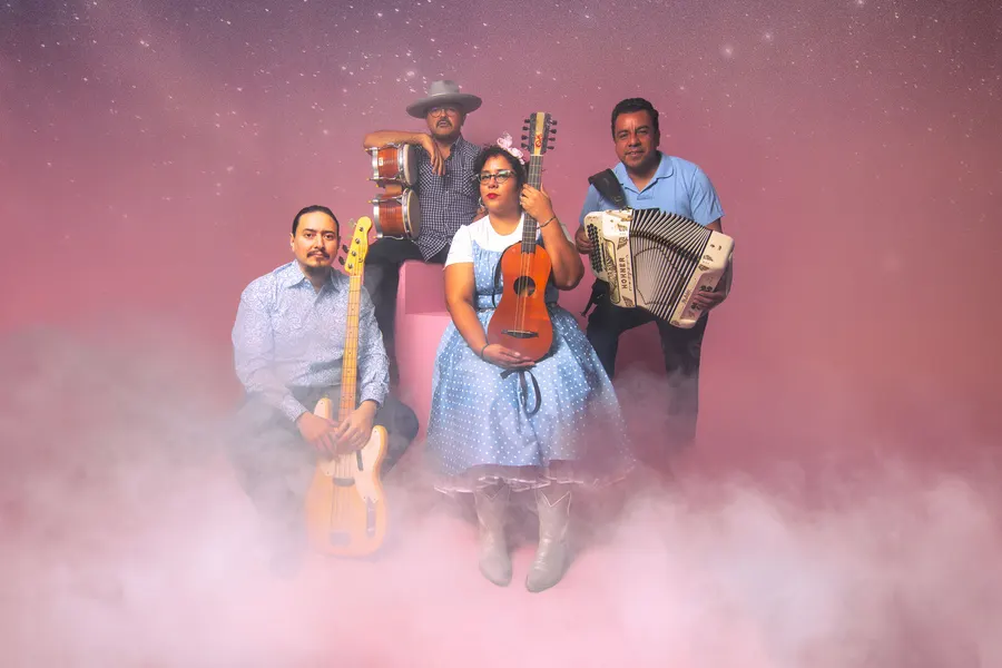 La Santa Cecilia with guitar, bass and accordion in pink fog