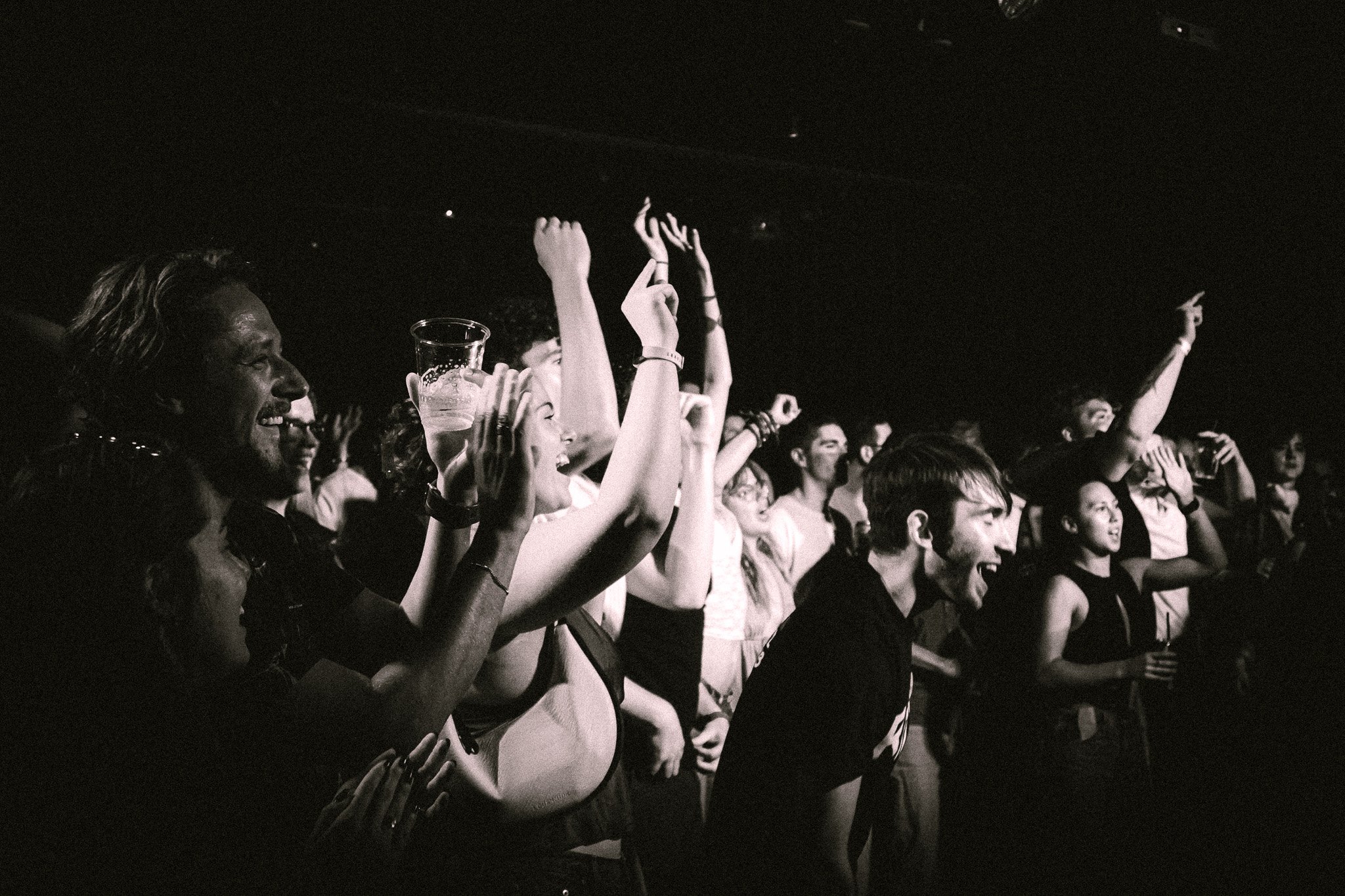 Black and white photo of a lively crowd at a concert, raising hands and cheering. bandkaroke.live