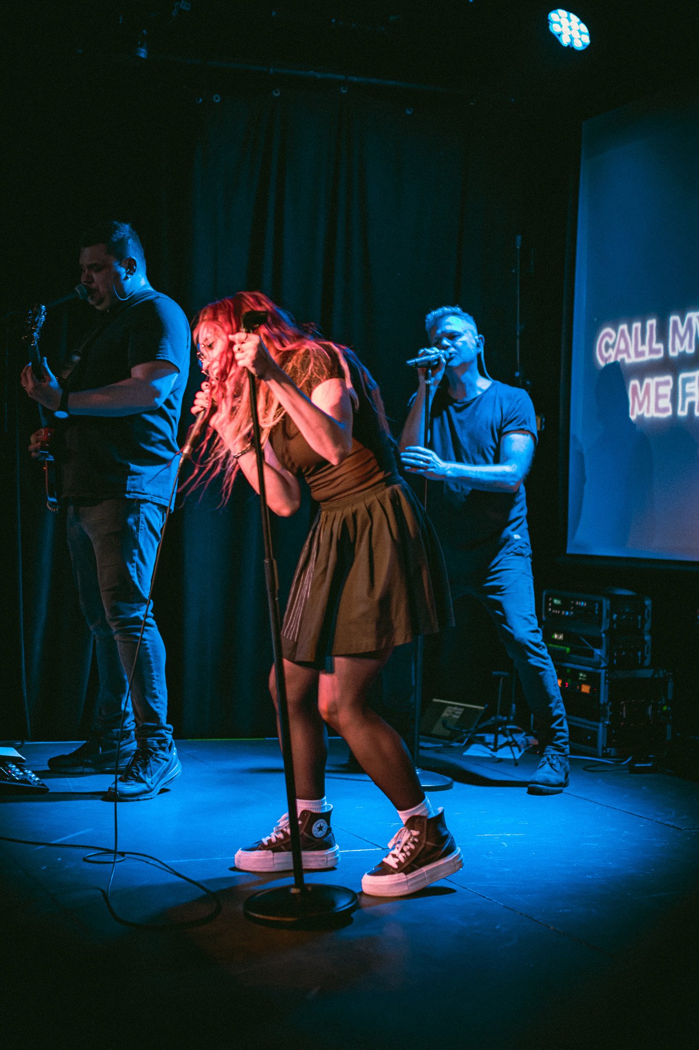 Three musicians performing on stage with microphones and guitar under blue lighting. bandkaroke.live
