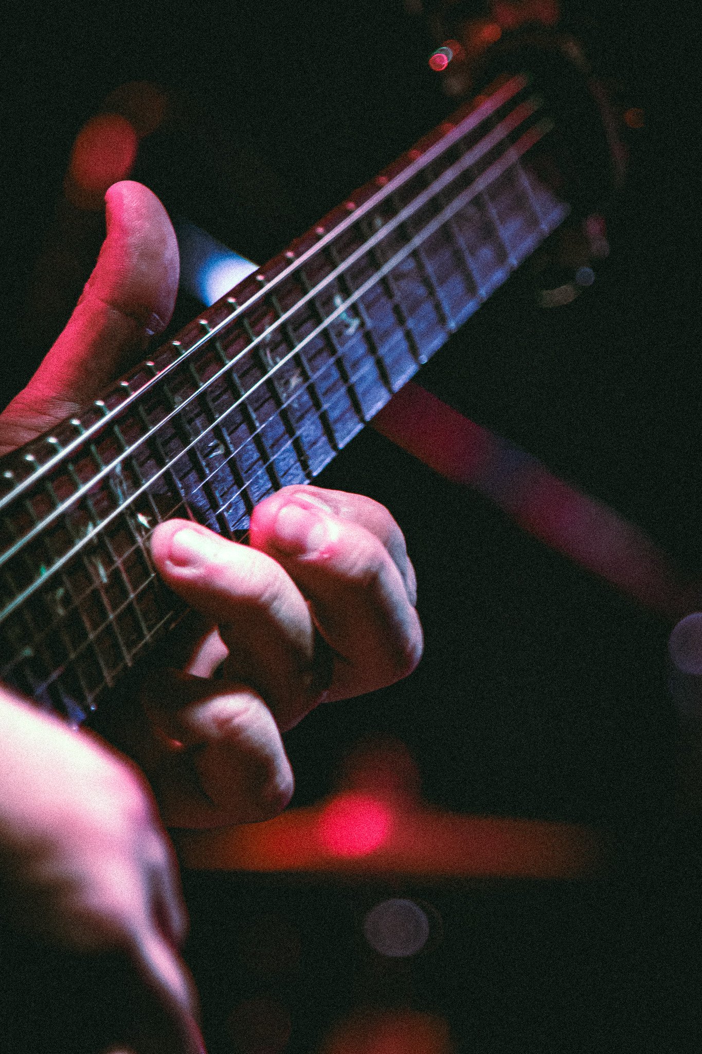 Close-up of a left hand playing a chord on the neck of an electric guitar with colorful stage lighting. bandkaroke.live