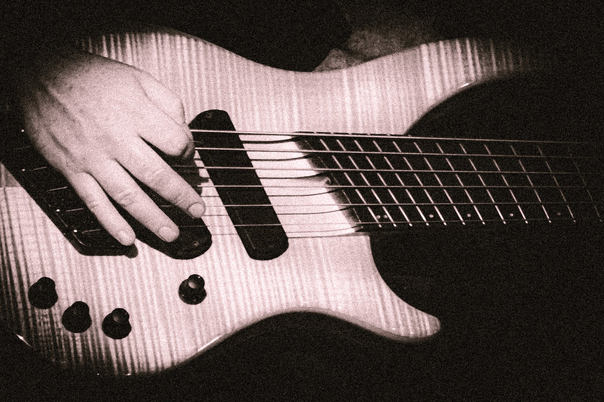Close-up of a hand playing an electric bass guitar with six strings in sepia tone. bandkaroke.live